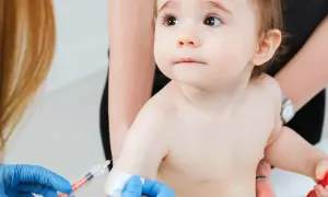 Małe dziecko otrzymuje szczepienie RSV. Ręka w niebieskiej rękawiczce trzyma strzykawkę, przygotowując się do podania zastrzyku.