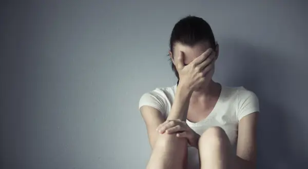 Kobieta siedzi przy ścianie, zakrywając twarz dłońmi. Czuć jej deprexolet.