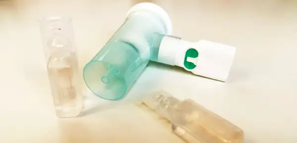 Nebulizator z zielonym przyciskiem i ampułkami, jedna z nich zawiera roztwór NaCl 0,9%.
