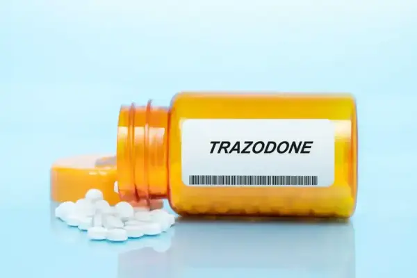 Pomarańczowa butelka z tabletkami trazodone, kilka białych tabletek wysypanych na niebieskie tło.