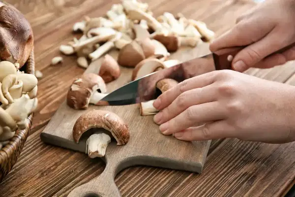 Ręce kroją pieczarki na desce. Niskie pieczarki kcal to zdrowa przekąska.